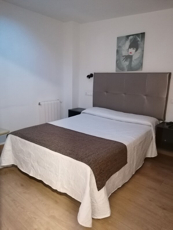 A bedroom with a bed, a nightstand, a wall-mounted lamp, and a painting. - Hostal Adelia (A Coruña)