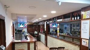 A bar area with wooden furniture, a counter, and shelves with bottles. - Hostal Adelia (A Coruña)