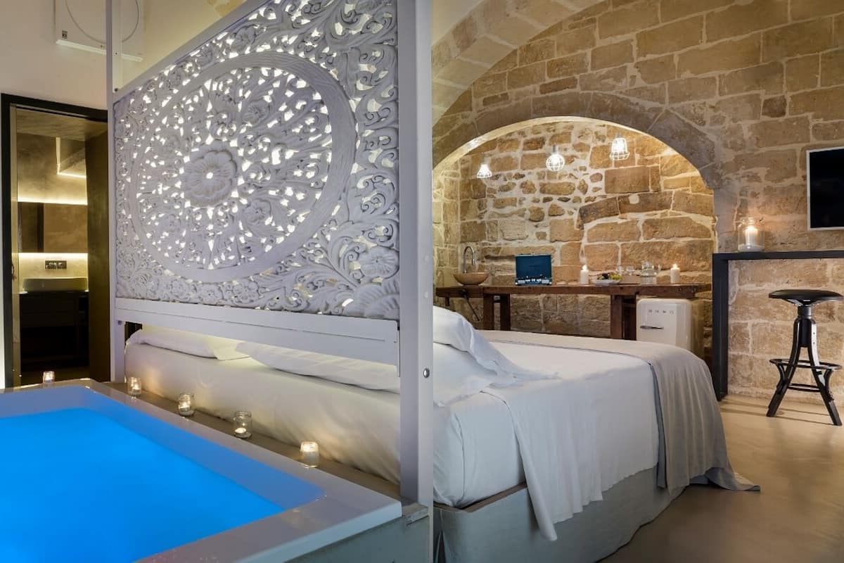 A bedroom with a large bed, a small bathroom, and a stone wall.