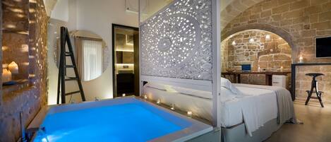 A bedroom with a large bed, a small bathroom, and a stone wall.