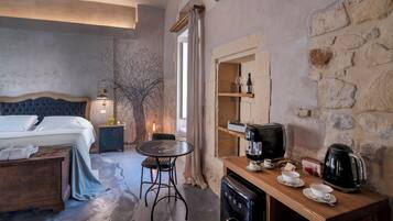 A bedroom with a bed, bedside table, and a small desk with a coffee maker and cups.
