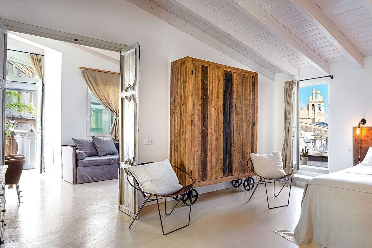 A hotel room with a large bed, two chairs, a wooden accent wall, and a view of the city.