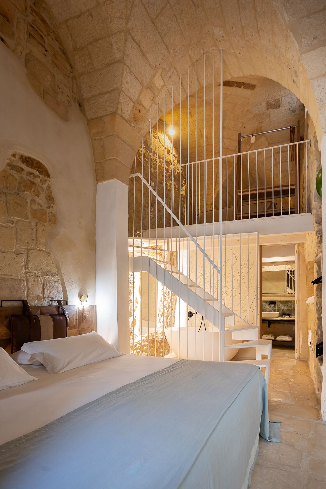 Ein Schlafzimmer mit Steinwand, einem Bett, einer Treppe und einer Küchenzeile.