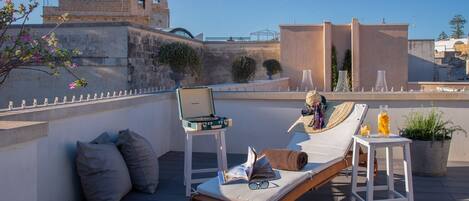 A rooftop terrace with lounge chairs, a portable record player, and a potted plant.