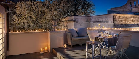 An outdoor patio with a dining table set for two, surrounded by wicker furniture and candles.