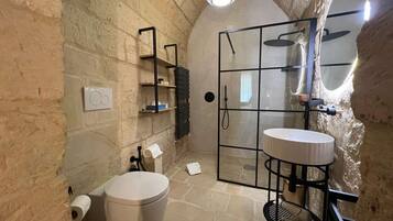 Une salle de bain avec un mur en pierre, une douche en verre, des toilettes et un lavabo doté d’un cadre noir.