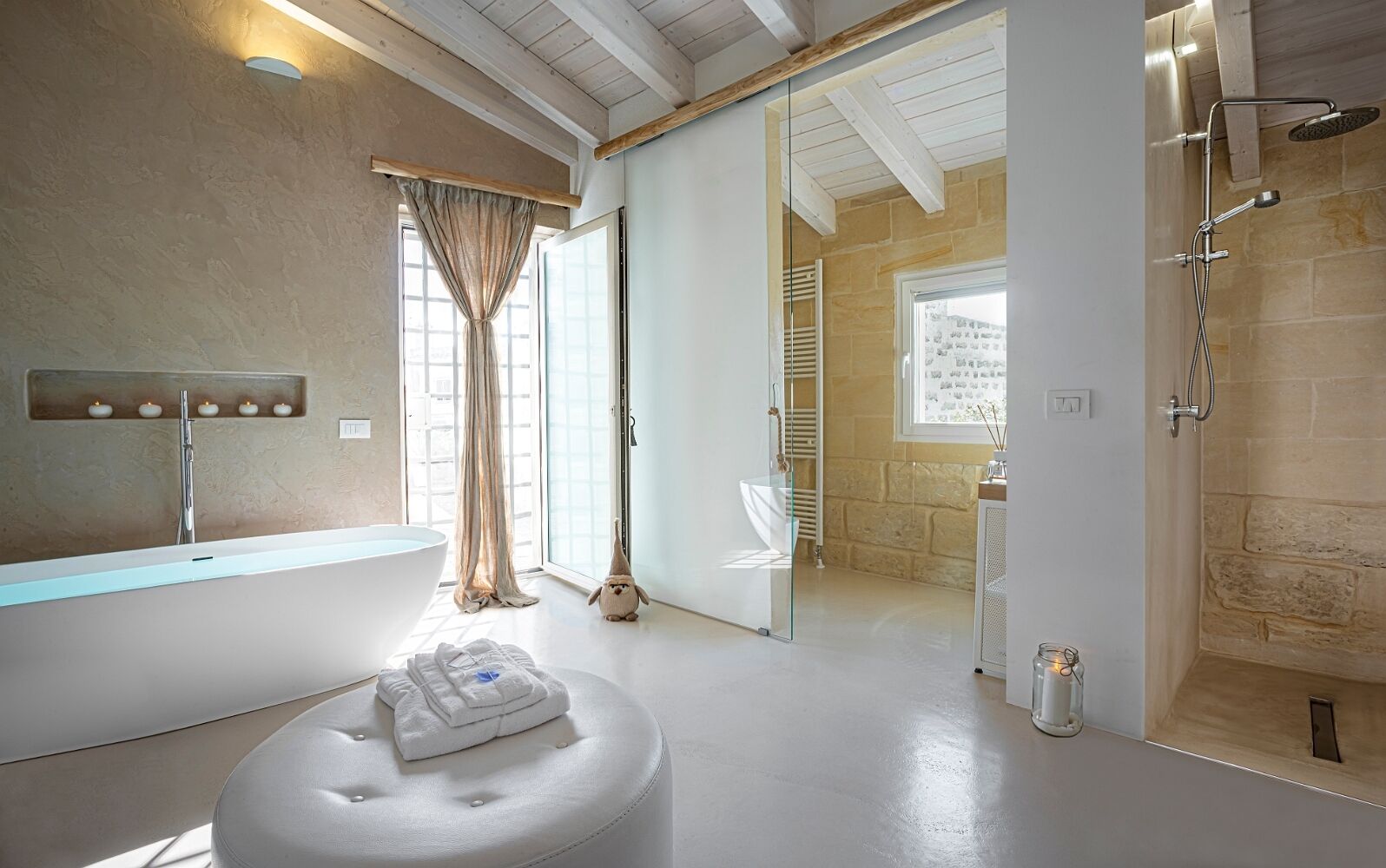 A modern bathroom with a freestanding bathtub, a glass shower enclosure, and a large window with curtains.