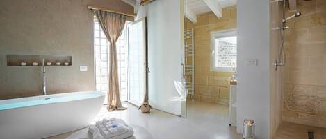 A modern bathroom with a freestanding bathtub, a glass shower enclosure, and a large window with curtains.