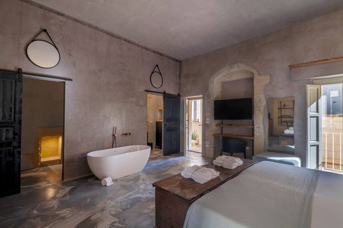 A spacious bathroom with a freestanding bathtub, a wooden bench with towels, and a stone archway.