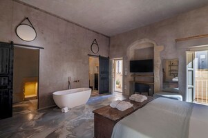 Un baño espacioso con una bañera independiente, un banco de madera con toallas y un arco de piedra.