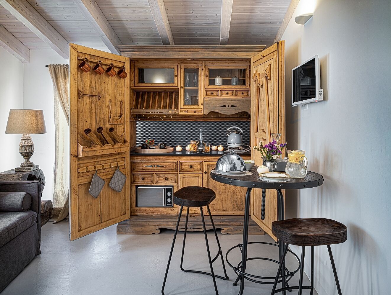 A compact kitchen with wooden cabinets, a built-in microwave, and a small dining area with stools.