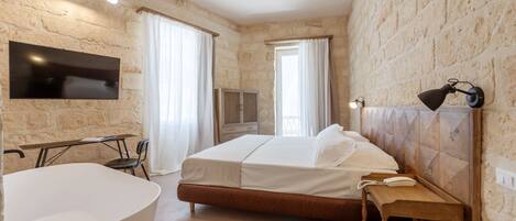 Une chambre avec un mur en pierre, un lit, une table de chevet, une lampe, un téléviseur et une fenêtre avec des rideaux.