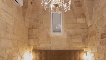 A bedroom with a stone wall, a wooden headboard, a chandelier, and a bed with white linens.
