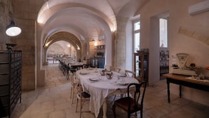 Uma sala de jantar com uma mesa comprida posta para uma refeição, paredes de pedra e tetos em arco.