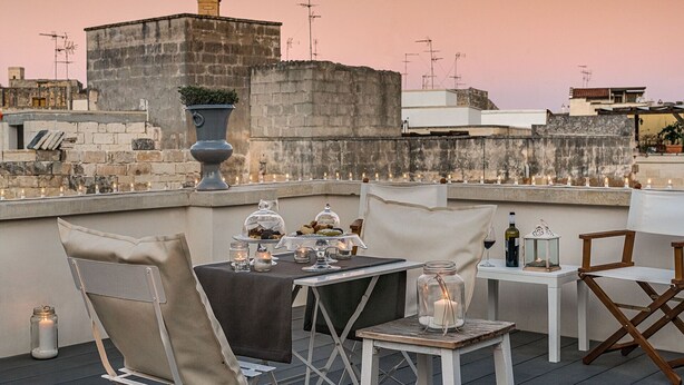 Terraço no telhado com uma mesa posta para refeições, rodeado de cadeiras e um vaso decorativo.
