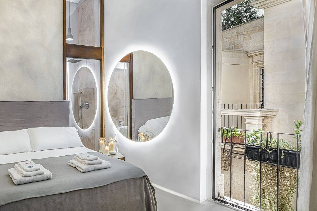 A modern bedroom with a large bed, two mirrors, a vanity with a sink, and a balcony with plants.