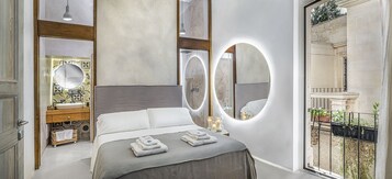 Un dormitorio moderno con una cama grande, dos espejos, un tocador con lavabo y un balcón con plantas.