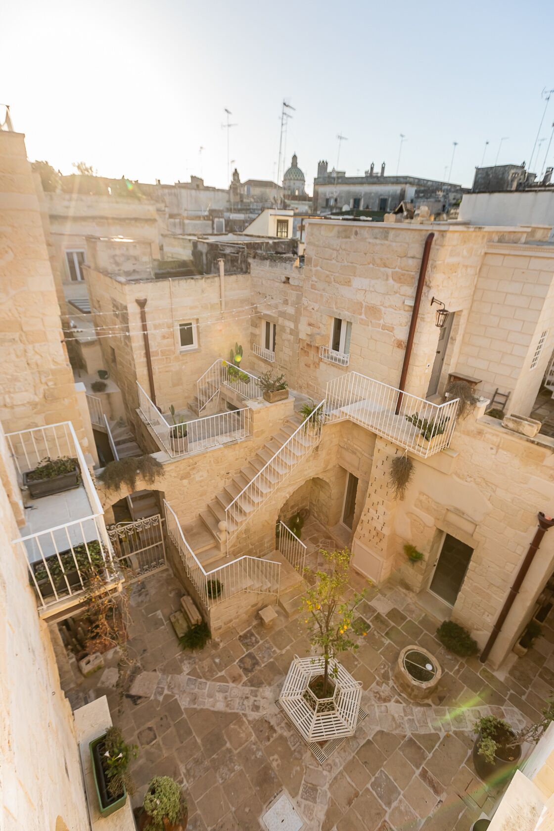 A courtyard with stone buildings, a central staircase, and potted plants.