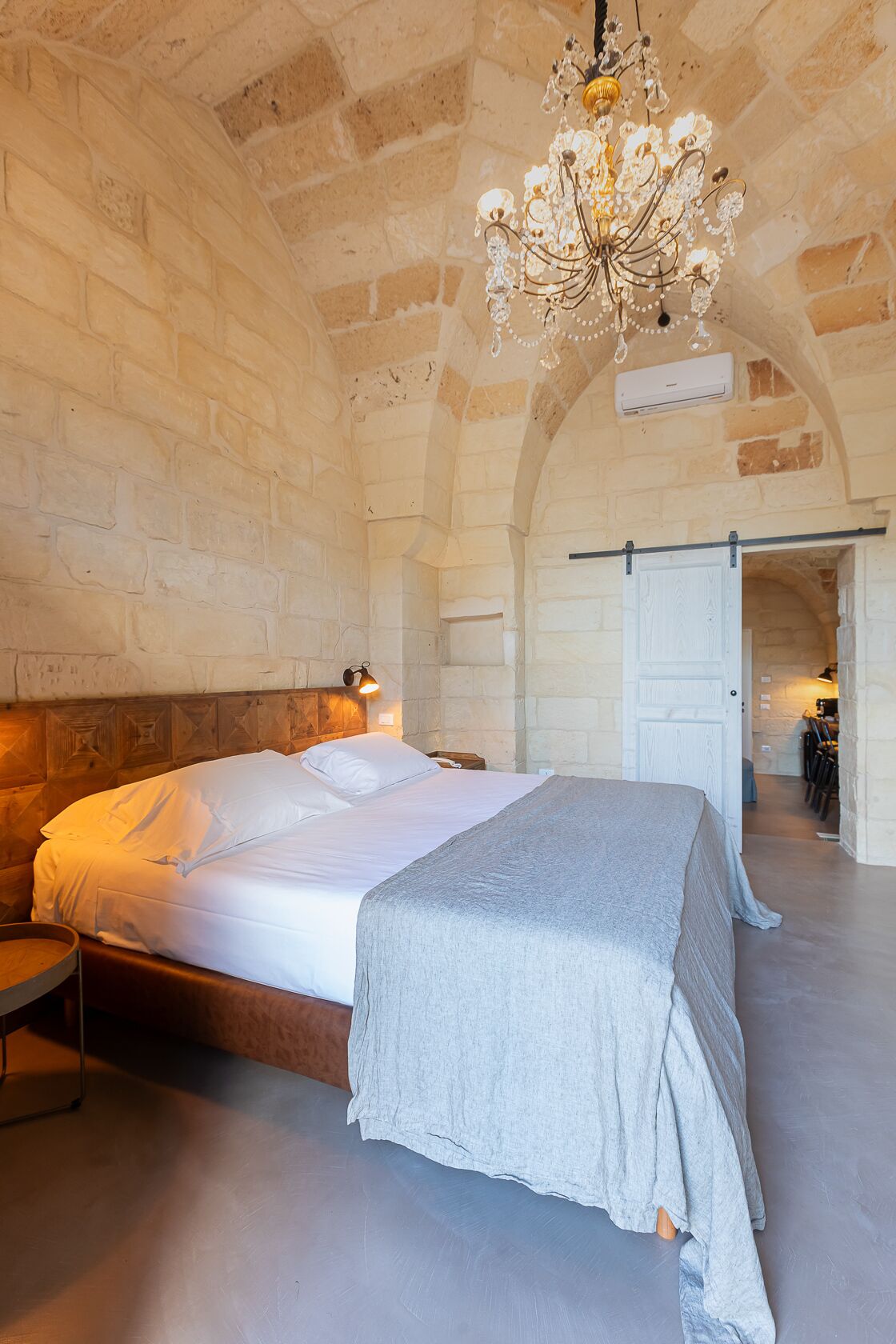 A bedroom with a large bed, a chandelier, stone walls, and an arched ceiling.