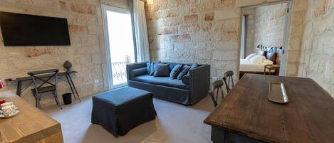 A cozy room with a sofa, a wooden table, a TV mounted on the wall, and a balcony with a view.