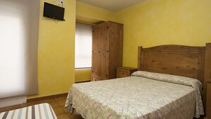 A bedroom with a bed, wooden wardrobe, bedside tables, and a television on the wall. - Hostal Velarde (Talavera de la Reina)