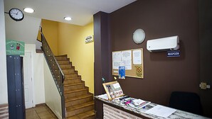 A reception area with a staircase, a clock, a bulletin board, and a reception desk. - Hostal Velarde (Talavera de la Reina)