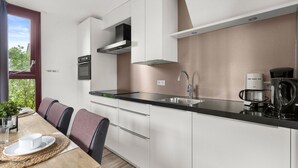 A modern kitchen with white cabinetry, a black countertop, and a built-in oven. There is a dining table with chairs and a coffee maker on the counter.