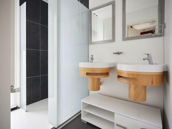 A modern bathroom with two sinks, a mirror, and a shower area.