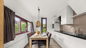 A modern kitchen with white cabinets, a black countertop, and a dining area with a wooden table and chairs.