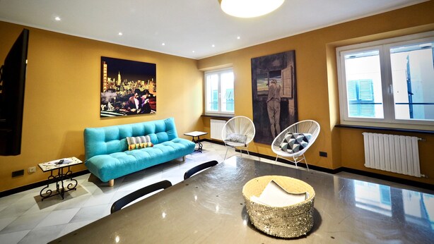 A modern living room with a blue sofa, two white armchairs, a round coffee table, and a large painting of a cityscape. - Lussuosa Dimora San Lorenzo (Genoa)