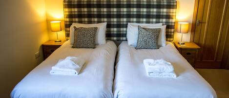 A hotel room with two beds, each with a pillow, a bedside lamp, and a folded towel.