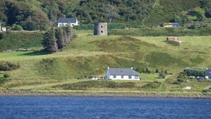 A coastal landscape with a prominent stone tower, several houses, and a body of water. - Old Pier Cottage B&B (Uig)