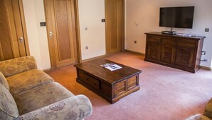 A living room with a sofa, a coffee table, a TV on a wooden cabinet, and two wooden doors. - Old Pier Cottage B&B (Uig)