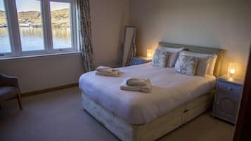 Un dormitorio con una cama grande, dos mesitas de noche, una butaca y una ventana con vistas a un lago.