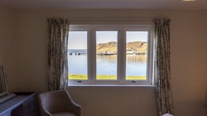 A room with a bed, a chair, and a window with a view of a body of water and hills. - Old Pier Cottage B&B (Uig)