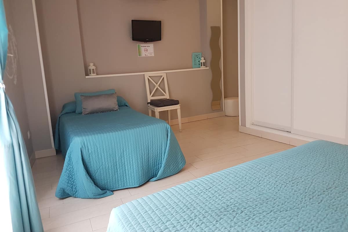 A bedroom with two beds, a small table, a chair, a TV, and a mirror.