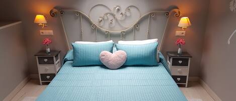 A bedroom with a skylight, a bed with teal bedding, heart-shaped pillows, and bedside tables with lamps and vases.