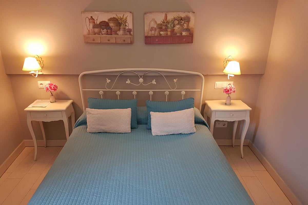 A bedroom with a bed, two nightstands, two lamps, and two wall-mounted pictures.
