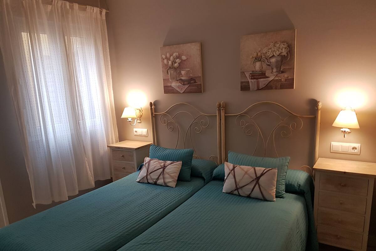 A double bed with two pillows, a nightstand with a lamp, and two wall-mounted paintings.