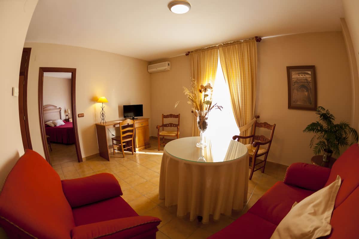 A living room with a round glass table, red sofas, a TV, and a potted plant.