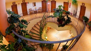 Una escalera de caracol con barandilla, rodeada de macetas con plantas y puertas de madera.