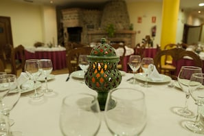 Una mesa de comedor dispuesta con copas de vino y platos, un farol decorativo y una chimenea de piedra al fondo.
