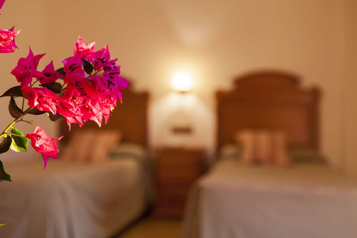 A hotel room with two beds, a nightstand, and a bedside lamp.
