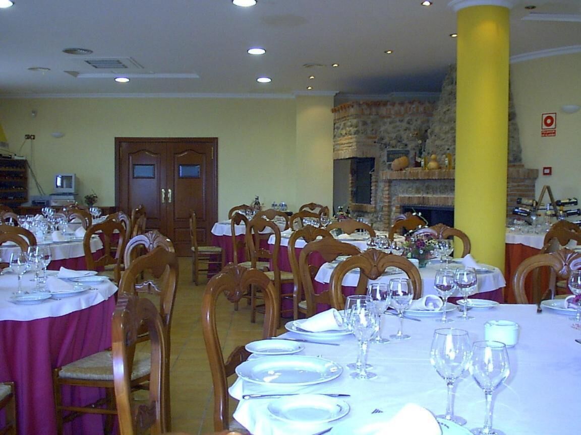 A dining area with multiple tables set for a meal, wooden chairs, and a stone fireplace in the background.