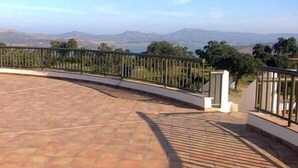 Una terraza en la azotea con barandilla curva, que ofrece vistas a colinas distantes y un cielo despejado.