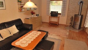 A cozy living room with a leather sofa, a wooden coffee table, a television on a stand, a fireplace, and a window with curtains.