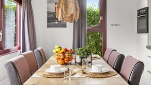 Un comedor con una mesa de madera, seis sillas, un frutero, dos tazas blancas y una lámpara colgante.