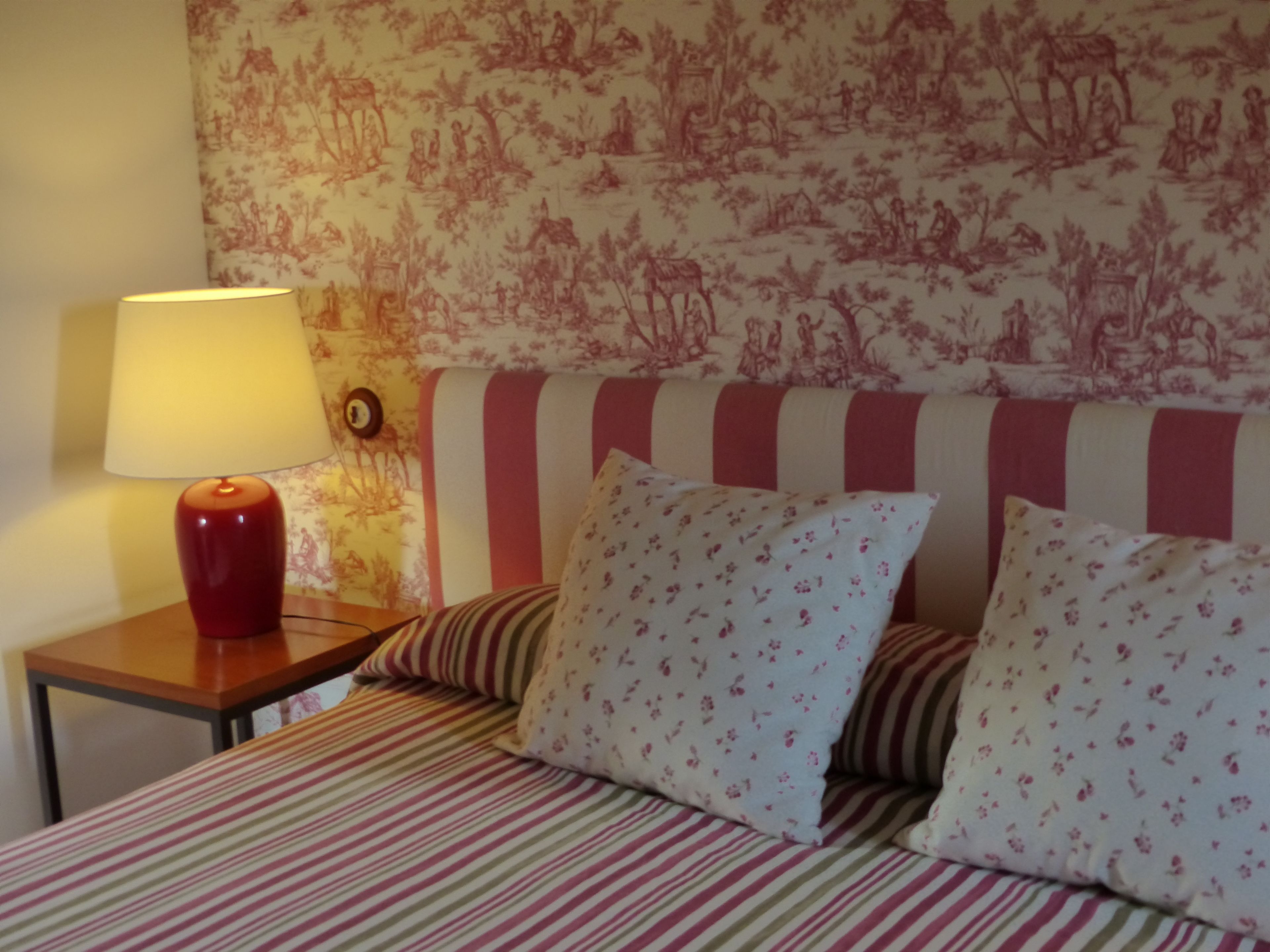 Un lit avec une literie à rayures, une lampe et un mur orné d’un motif floral.