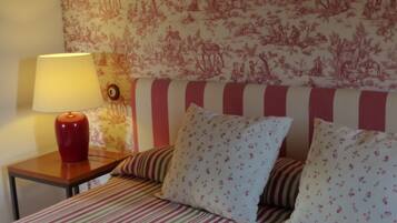 Un lit avec une literie à rayures, une lampe et un mur orné d’un motif floral.