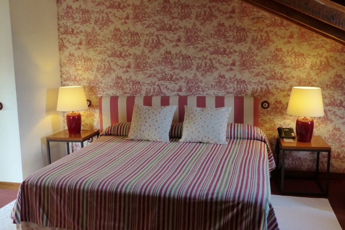 A bedroom with a striped bedspread, two bedside lamps, and floral wallpaper.